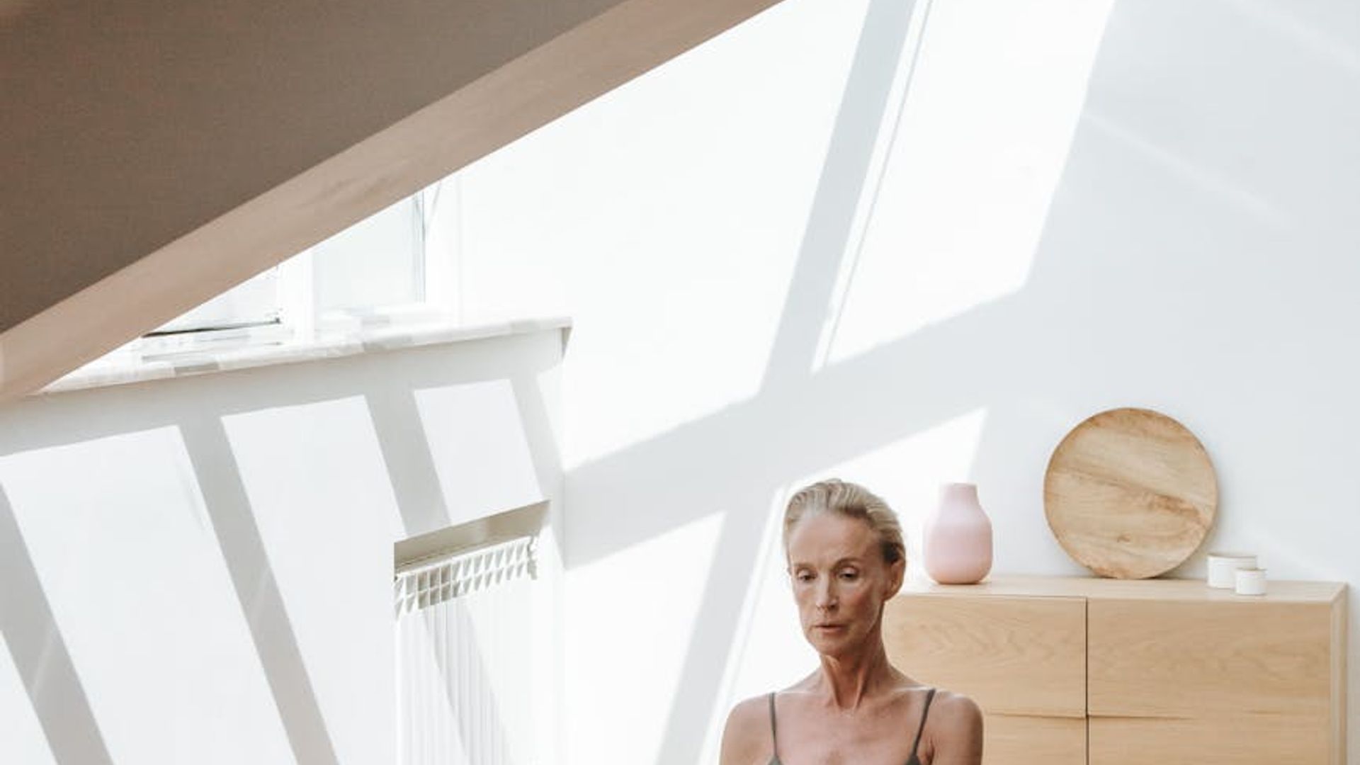Person practicing gentle yoga in a bright minimalistic studio with wooden floor.